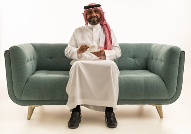 رجل سعودي بالزي التقليدي يجلس على الأريكة مع قهوة