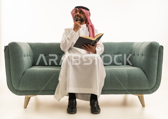 رجل سعودي يقرأ كتاب على الأريكة بتفكير