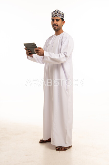رجل عماني يحمل جهاز لوحي على خلفية بيضاء