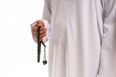 رجل عربي يرتدي الثوب التقليدي ويمسك مسبحة سوداء بخلفية بيضاء