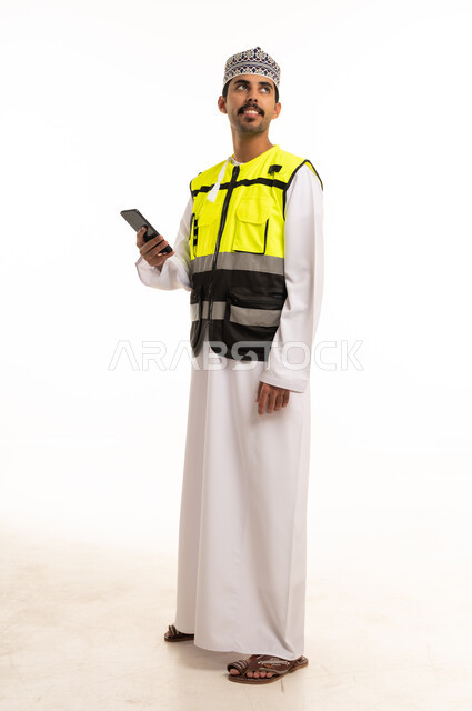 An Omani engineer in safety attire holding a mobile phone.
