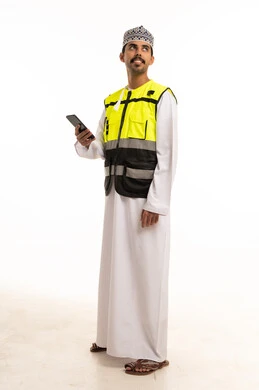 An Omani engineer in safety attire holding a mobile phone.