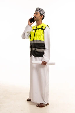 An Omani engineer in safety attire holding a mobile phone.