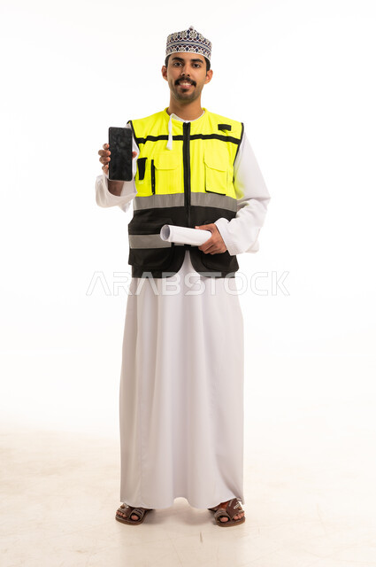 An Omani engineer in safety attire holding a mobile phone.
