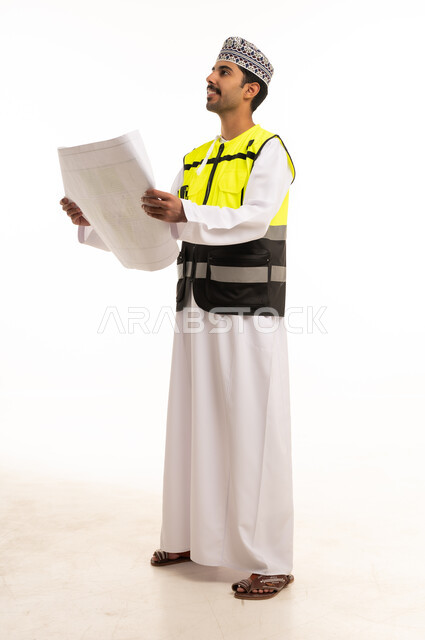 مهندس عماني يحمل مخططاً معمارياً بسترة السلامة