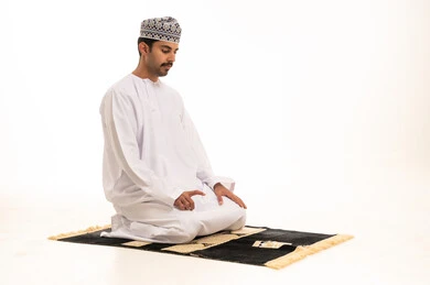 رجل عُماني يصلي على سجادة صلاة خلفية بيضاء