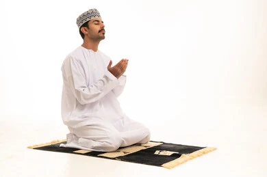 رجل عُماني يصلي على السجادة بخلفية بيضاء