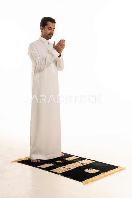 رجل سعودي يرتدي الثوب الأبيض يدعو على سجادة صلاة