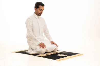 رجل سعودي يصلي على السجادة بخلفية بيضاء