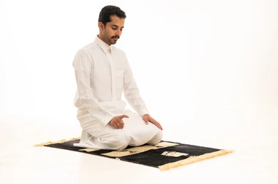 رجل سعودي بالثوب يصلي على السجادة خلفية بيضاء