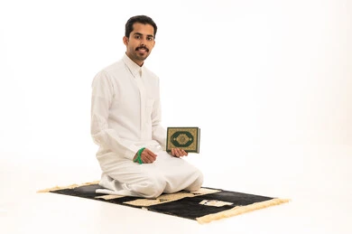 رجل سعودي يحمل القرآن الكريم على سجادة الصلاة