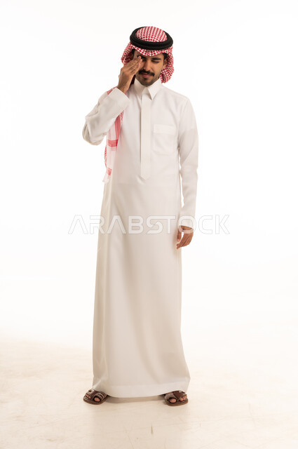 رجل سعودي بالثوب يفرك عينه على خلفية بيضاء