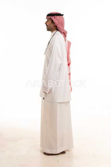 A Saudi doctor in traditional attire and a coat in front of a white background.