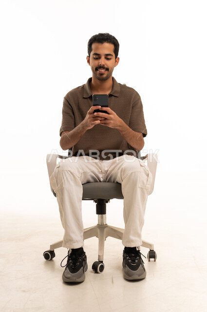 شاب سعودي يجلس على كرسي مكتب يستخدم الجوال