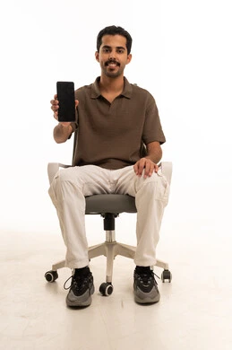 رجل عربي يجلس على كرسي مكتب يحمل شاشة هاتف فارغة