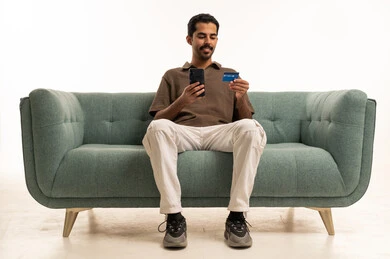 Saudi Man Using Smartphone and Credit Card on Sofa