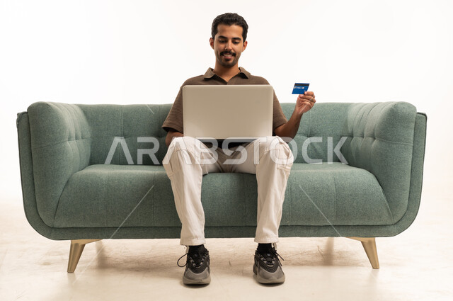 رجل سعودي مع لابتوب وبطاقة ائتمان على الأريكة