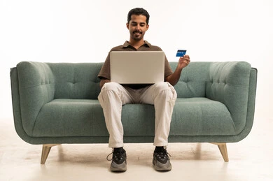 رجل سعودي مع لابتوب وبطاقة ائتمان على الأريكة