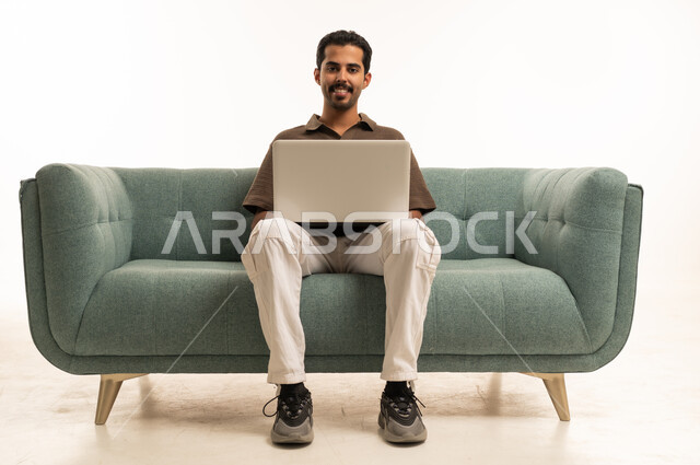 رجل عربي مبتسم يستخدم الحاسوب المحمول على أريكة