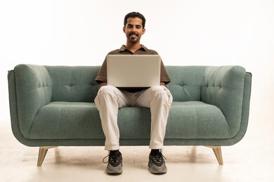 رجل عربي مبتسم يستخدم الحاسوب المحمول على أريكة