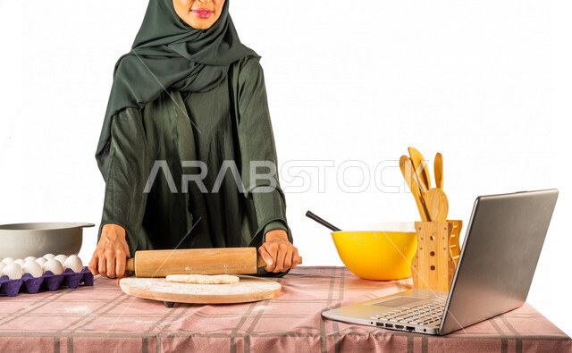 بورتريه لمرأة خليجية سعودية، تقف أمام طاولة عليها مكونات خاصة بالعجين وأواني الخبز وأدوات خاصة بالمطبخ والعجين، إعداد المخبوزات الشهية، إستخدام جهاز الحاسوب المحمول، بث مباشر، مشاركة تحضير الوصفات على مواقع التواصل الاجتماعي، إستخدام أجهزة تقنية حديثة