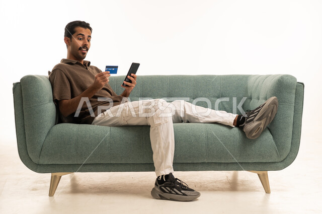 Saudi Man Using Credit Card and Smartphone on Sofa