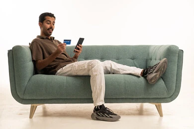 Saudi Man Using Credit Card and Smartphone on Sofa