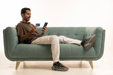 Arab Man Using Credit Card and Smartphone on Sofa