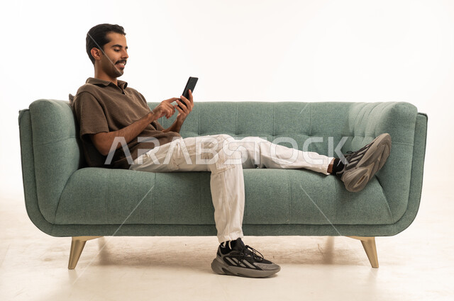 رجل سعودي يستخدم الهاتف الذكي على أريكة حديثة