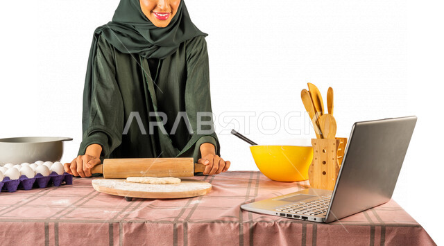 بورتريه لمرأة خليجية سعودية، تقف أمام طاولة عليها مكونات خاصة بالعجين وأواني الخبز وأدوات خاصة بالمطبخ والعجين، إعداد المخبوزات الشهية، إستخدام جهاز الحاسوب المحمول، بث مباشر، مشاركة تحضير الوصفات على مواقع التواصل الاجتماعي، إستخدام أجهزة تقنية حديثة