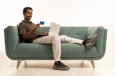 رجل عربي يستخدم المحمول وبطاقة الائتمان على الأريكة