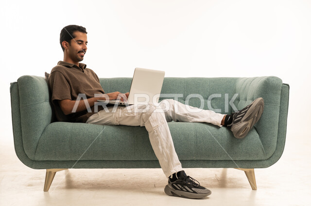 رجل سعودي يستخدم الكمبيوتر المحمول على الأريكة