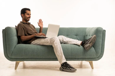 Arab Man Waving at Laptop During Video Call on Sofa