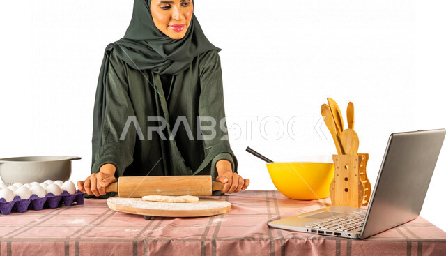 Portrait of a Saudi Gulf woman, standing in front of a table with ingredients for dough, baking utensils, kitchen and dough tools, preparing delicious baked goods, using a laptop, broadcasting live, sharing recipes on social media, using modern technical