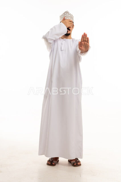 رجل عماني يشير بالتوقف ويغطي عينيه في الاستوديو