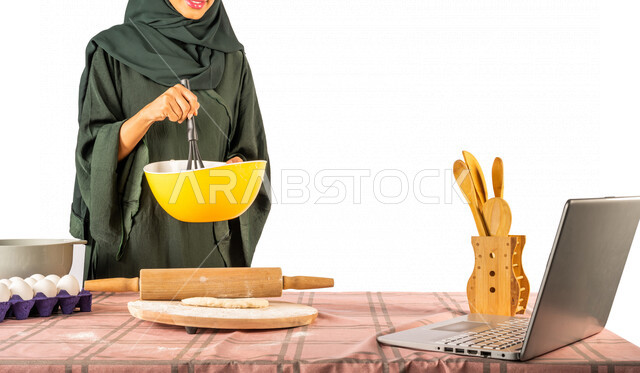 بورتريه لمرأة خليجية سعودية، تقف أمام طاولة عليها مكونات خاصة بالعجين وأواني الخبز وأدوات خاصة بالمطبخ والعجين، إعداد المخبوزات الشهية، إستخدام جهاز الحاسوب المحمول، بث مباشر، مشاركة تحضير الوصفات على مواقع التواصل الاجتماعي، إستخدام أجهزة تقنية حديثة