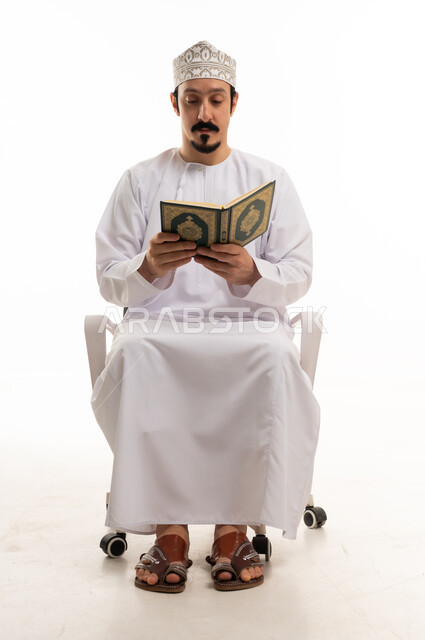 رجل عُماني يرتدي الزي التقليدي يقرأ القرآن الكريم