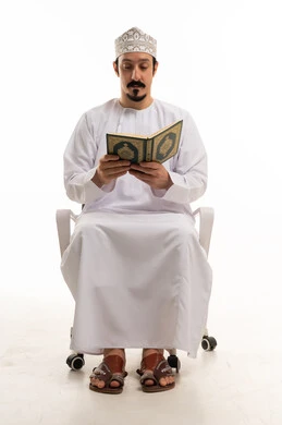 رجل عُماني يرتدي الزي التقليدي يقرأ القرآن الكريم