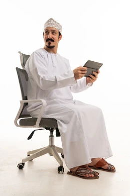رجل عُماني بجهاز لوحي يجلس على كرسي مكتب