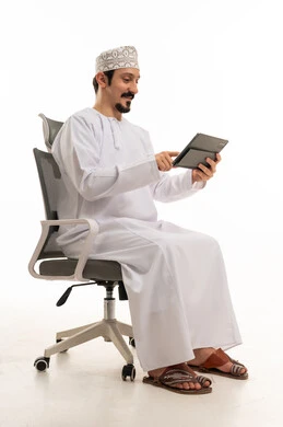 رجل عماني يستخدم جهاز لوحي على كرسي مكتب