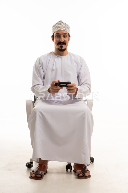 رجل عماني يمسك بجهاز تحكم ألعاب بخلفية بيضاء