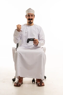 رجل عماني يمسك بجهاز تحكم الألعاب ويرفع قبضة الفوز