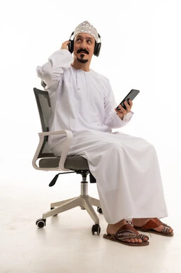 رجل عُماني يرتدي سماعات رأس ويستخدم هاتفه الذكي
