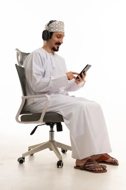 رجل عماني بالزي التقليدي يستخدم الهاتف وسماعات الرأس