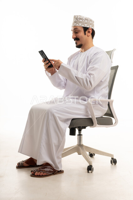 رجل عماني يستخدم الهاتف الذكي على كرسي مكتب بخلفية بيضاء