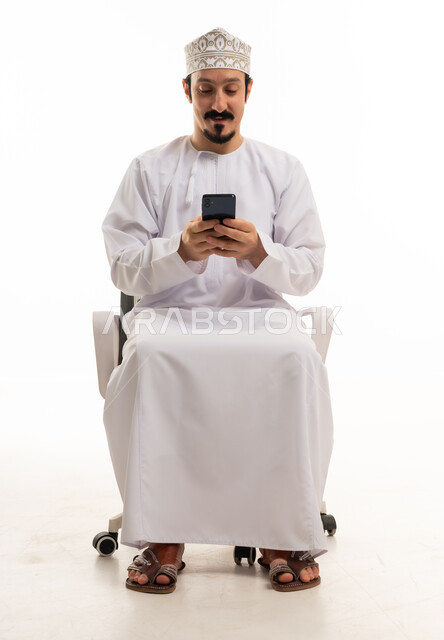 رجل عماني يستخدم الهاتف الذكي على كرسي مكتب