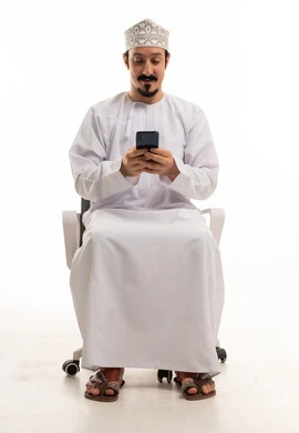 رجل عماني يستخدم الهاتف الذكي على كرسي مكتب
