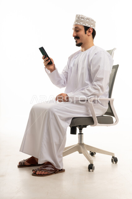 Omani Man Sitting on Office Chair Using Smartphone