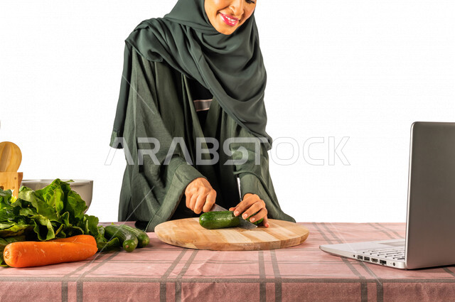 Portrait of a Saudi Gulf woman, standing in front of a table with a group of fresh vegetables, making a video call via a laptop, sharing preparing recipes on social media, preparing salads and healthy dishes, the concept of a healthy diet, live broadcast
