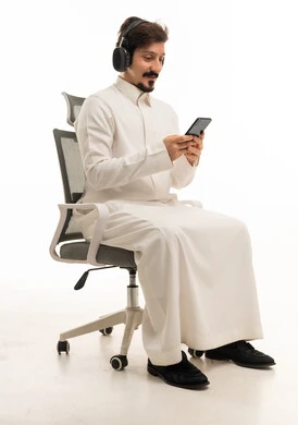 رجل سعودي يرتدي سماعات ويستخدم الجوال على كرسي مكتب